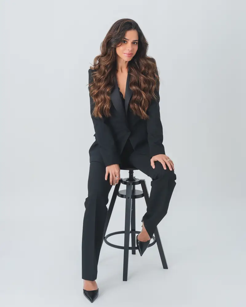 Priscilla Jorge sentada num banco alto, de terno preto